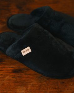 Pantufa Silver Preta, par felpudo com etiqueta Pinuk na lateral, sobre piso de madeira