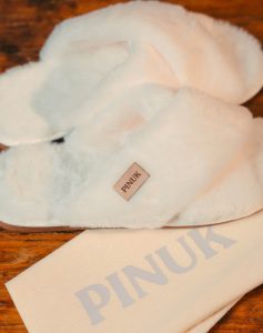 Pantufa Anatômica X Branca felpuda de tiras cruzadas sobre madeira, com saquinho de tecido Pinuk