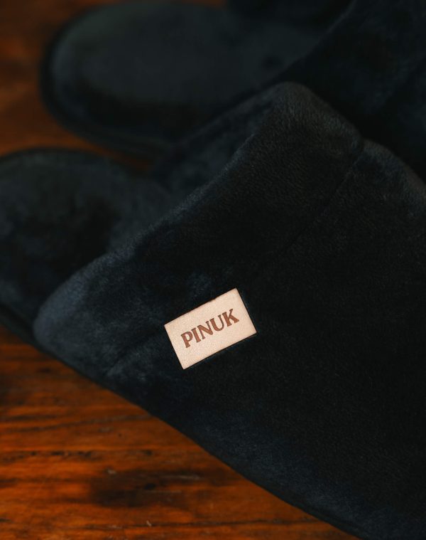 Pantufa Silver Preta em detalhe, com textura felpuda e etiqueta Pinuk, sobre piso de madeira