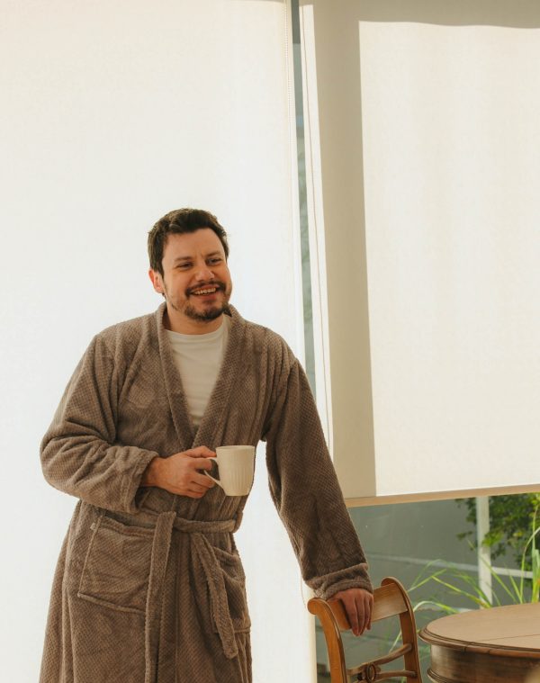 Roupão Polo Mineral vestido por homem sorridente com caneca, apoiado em cadeira de madeira
