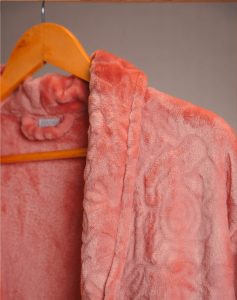 Roupão Lady Blush rosa-coral felpudo com relevo floral pendurado em cabide de madeira