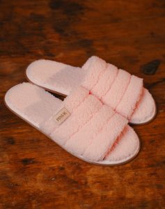 Pantufa Pespontada Rosa, par felpudo aberto na frente com gomos acolchoados sobre piso de madeira rústica